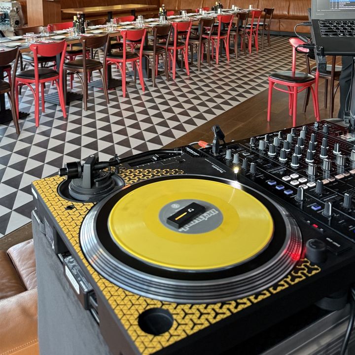 Gramofon z żółtą płytą winylową w restauracji, w tle nakryty długi stół